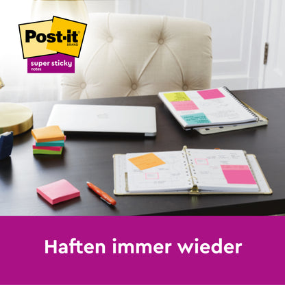 Ein moderner Schreibtisch mit Stapeln von 3M Deutschland GmbH Post-it® Super Sticky Notes Würfel in Gelb (76 mm x 76 mm), einem aufgeklappten Laptop, Planern mit angehefteten Notizen, einem Stift und einer Lampe. Das Logo befindet sich oben links. Text: "Haften immer wieder.