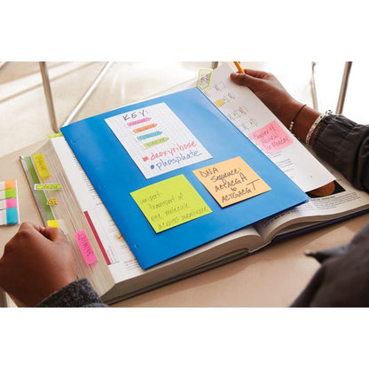 Osoba študuje na pracovnom stole s otvorenou učebnicou, modrou zložkou a farebnými Post-it® Notes Energetic Collection (38x51 mm) od 3M Deutschland GmbH. Poznámky a tabuľka na zložke poskytujú biologické pripomienky, zatiaľ čo osoba drží pero a knihu.