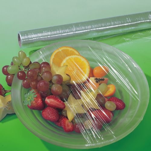 Priehľadný list Starpak potravinovej fólie (30 m x 29 cm) pokrýva tanier so zmiešaným ovocím. V pozadí je na zelenej ploche vidieť odolnú Starpak potravinovú fóliovú rolku v jej skladacej škatuľke (1 kus).