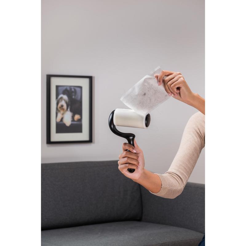Osoba odlupuje použitý list zo Scotch-Brite™ Everyday Clean Fusselroller na ploché povrchy (56 listov, 1/balenie) od 3M Deutschland GmbH, zatiaľ čo stojí pred sivým gaučom a fotografiou psa - ideálne na čistenie plochých povrchov.
