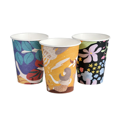 Three Art Series Kaffeebecher von Duni GmbH: PAP/PLA bedruckt mit blauen, violetten Blättern, einer sitzenden Person auf Gelb und bunten Blumen auf Schwarz - stilvoll, biologisch abbaubar und umweltfreundlich.
