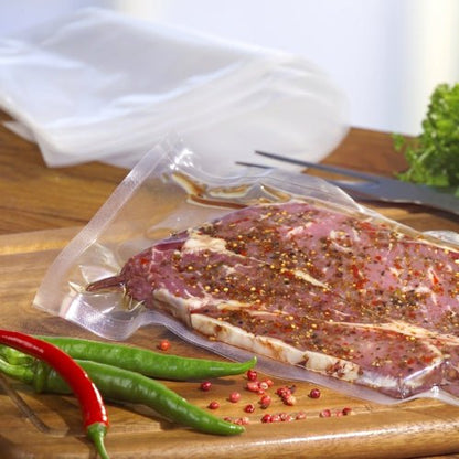 Starpak 100 Siegelrandbeutel, PA/PE transparentný od Starpak drží marinované surové mäso na drevenej doske so zelenými a červenými čili papričkami, kliešťami a listovou zeleninou - ideálny pre váš komorový vákuovač.