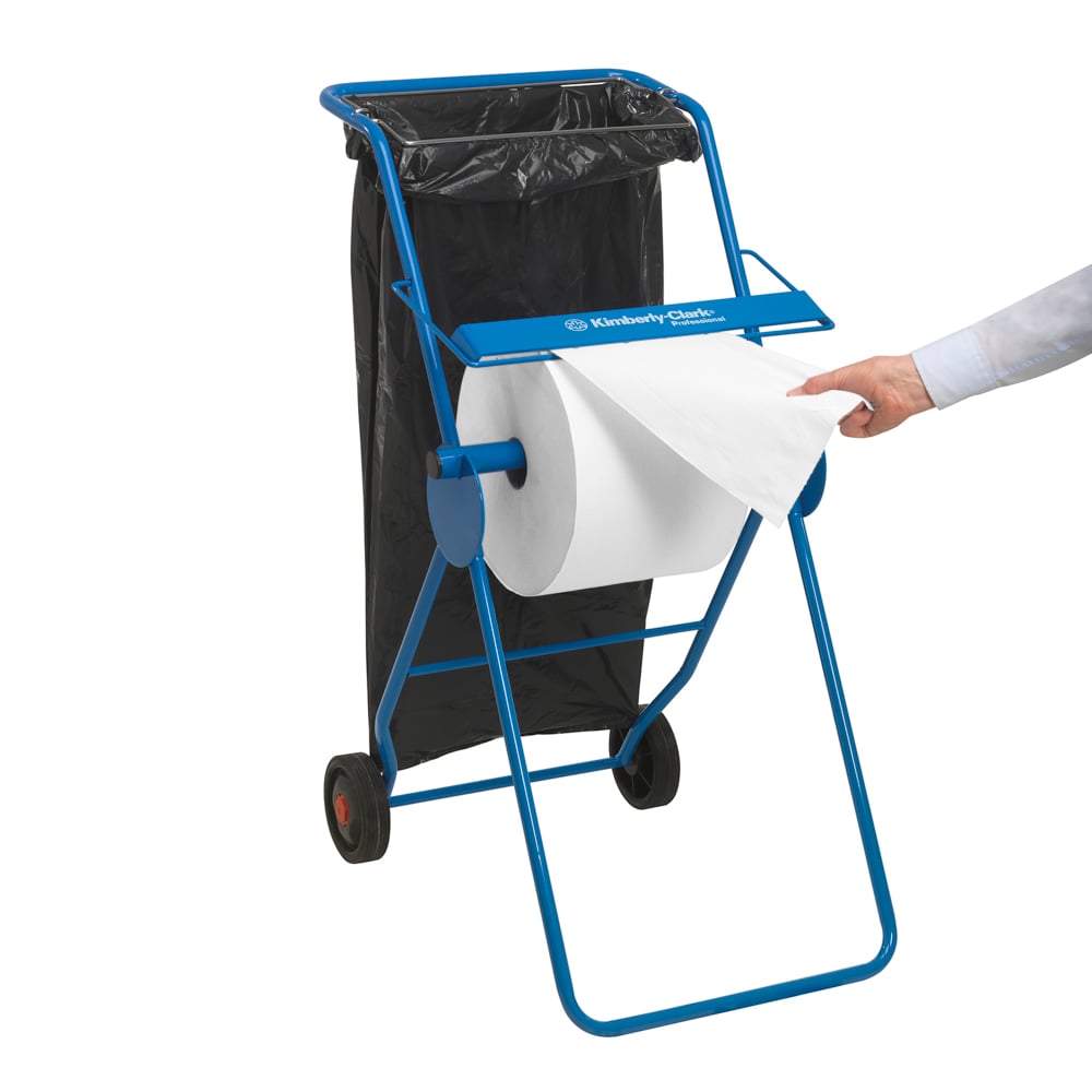 Mobilný modrý dávkovač s dvoma kolesami drží veľkú rolku utierok WypAll® L10 EXTRA (biela, 1500 listov) od Kimberly-Clark GmbH; čierny odpadkový vak je pripevnený, zatiaľ čo jedna ruka ťahá list z veľkej rolky.