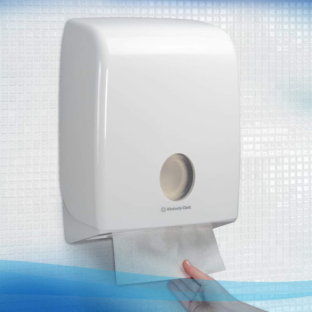 Ruka vyberá savý Scott® CONTROL™ skladací uterák od Kimberly-Clark GmbH z bieleho nástenného dávkovača na hygienické sušenie rúk, namontovaného na dlaždenej stene.