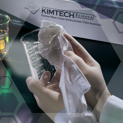 Osoba s bielymi rukavicami utiera čistý sklenený pohár s precíznymi utierkami Kimtech® Science od Kimberly-Clark GmbH. V pozadí je škatuľa s utierkami (100 listov, 2-vrstvové) a pohár s tekutinou.