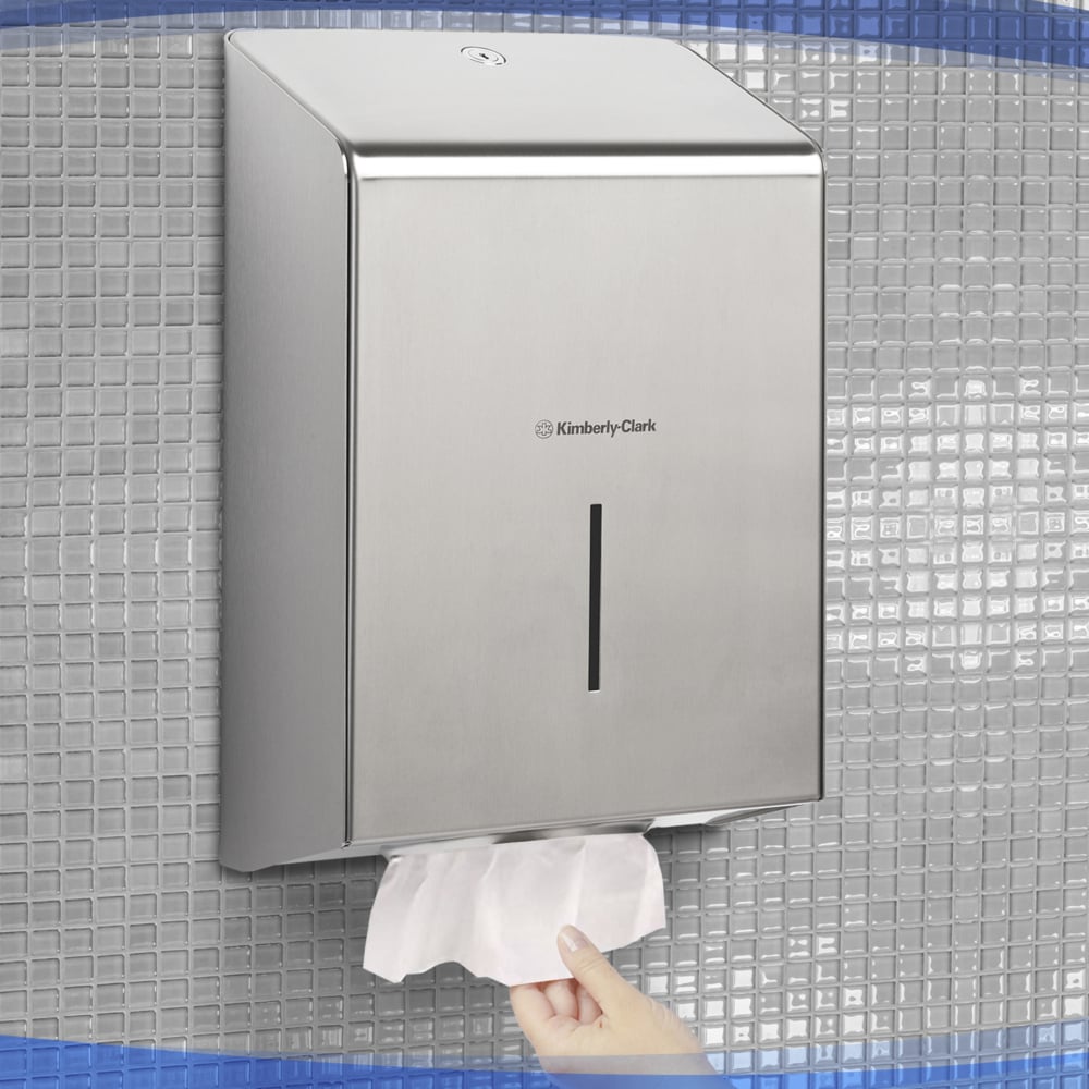 Ruka ťahá papierový uterák z dávkovača uterákov Kimberly-Clark Professional™ z nehrdzavejúcej ocele (1 dávkovač), hygienicky namontovaného na obloženej stene.