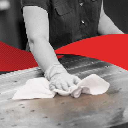 Osoba v krátkorukávovej košeli utiera veľkú kovovú plochu handrou, možno WypAll® X60 General Clean od spoločnosti Kimberly-Clark GmbH z krabice BRAG™ (41,80 cm x 28,30 cm); obrázok je prevažne čiernobiely s výraznou červenou diagonálou v strede.