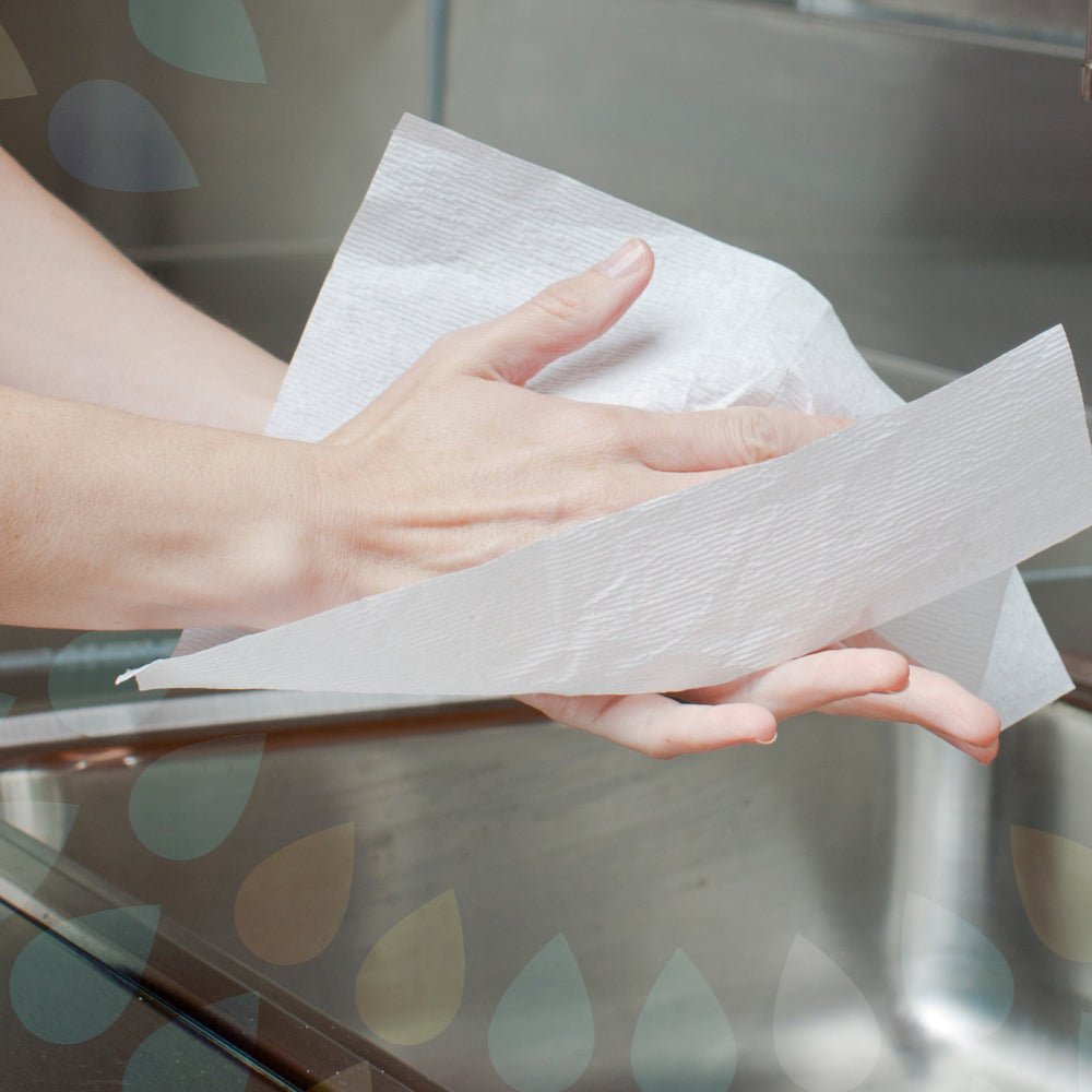 Osoba si suší ruky s Kleenex® uterákmi - MultiFold / Biele od Kimberly-Clark GmbH nad kovovým umývadlom, pričom polopriehľadné kvapky vody v pozadí vytvárajú svieži, moderný pocit umyvárne.