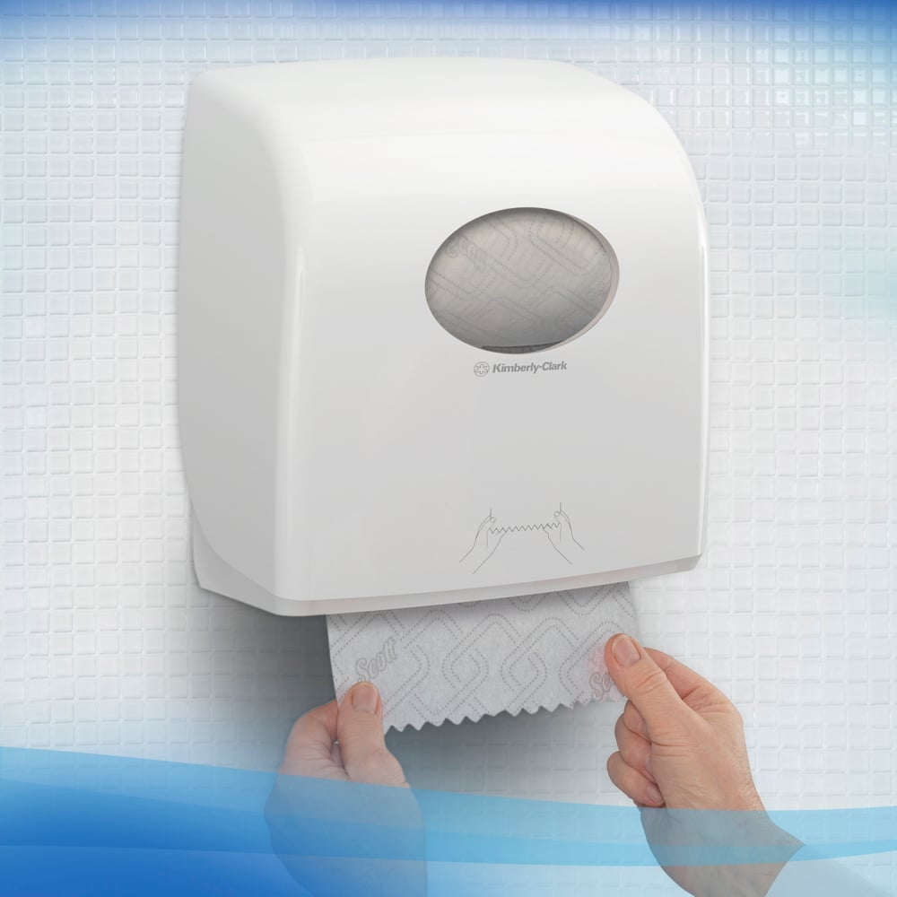 Osoba vyťahuje Scott® CONTROL EXTRA STRONG utierky z bieleho nástenného dávkovača od Kimberly-Clark GmbH, ktorý stojí na bielych, štruktúrovaných dlaždiciach. Na prednej strane dávkovača roliek utierok je zobrazený jednoduchý návod na použitie.