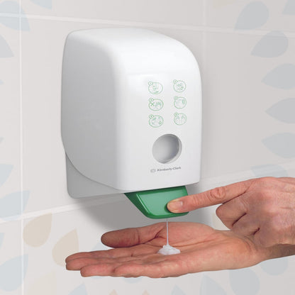 Osoba dávkuje Kleenex® hydratačný krém na ruky a telo (Kimberly-Clark GmbH) z bielej jednolitrovej nástennej kazety v kúpeľni s dlažbou so zelenou pákou pre starostlivosť o ruky a telo. Balenie: 6 kaziet na kartón.