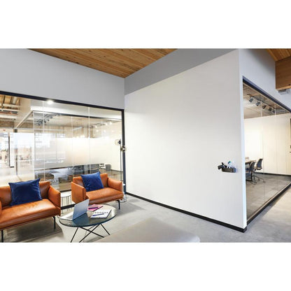 Moderný kancelársky čakací priestor s dvoma hnedými koženými kreslami, modrými vankúšmi, skleneným konferenčným stolíkom s notebookom a poznámkovým blokom a sklenenými rokovacími miestnosťami, ktoré sú vybavené Post-it® Easy Erase Whiteboard povrchom od 3M Deutschland GmbH.