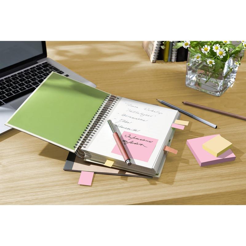 Špirálový zápisník s ručne písanými poznámkami, perom a Post-it® Recycling Notes 76x76 mm (100% PEFC, 100 listov/blok) od 3M Deutschland GmbH leží otvorený na drevenom stole vedľa notebooku, ceruzky, zatvoreného zápisníka a vázy s kvetmi.