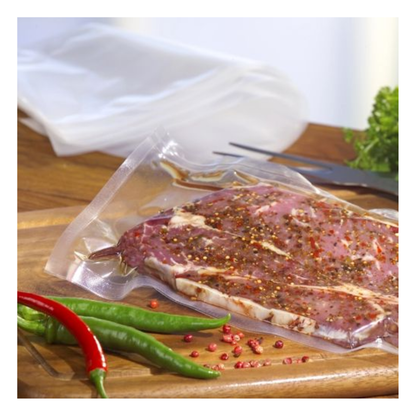 Surový, marinovaný steak je vákuovaný v priehľadnom Starpak 100 zatavovacom vrecku (PA/PE) s komorovým vákuovačom na drevenej doske, s chilli papričkami, ružovým korením, listovou zeleninou a vidličkou v pozadí.