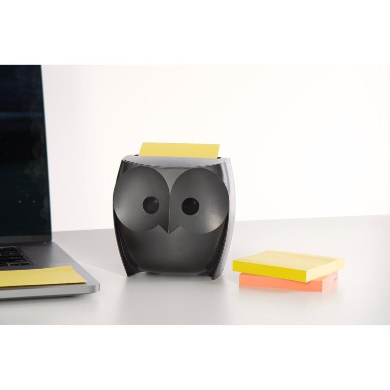Dávkovač 3M Post-it® Z-Notes v tvare sovy, čierny, drží žlté Super Sticky Z-Notes. Vedľa leží zatvorený laptop a balenie so žltými a ružovými Z-Notes (2 bloky po 45 listov) na bielom stole.