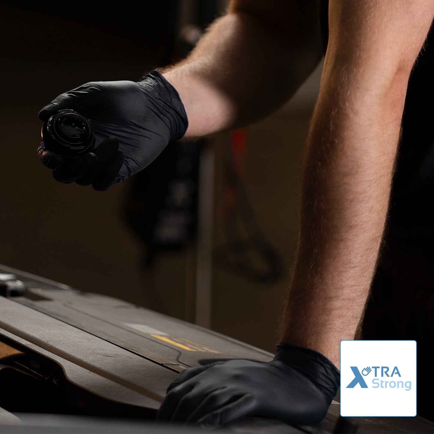 Eine Person, die ARNOMED NITRIL BLACK XTRA STRONG Einmalhandschuhe aus Nitril von ARNOWA GmbH in Schwarz trägt, arbeitet am Auto. Im Bild ist das "XTRA Strong" Logo sichtbar.