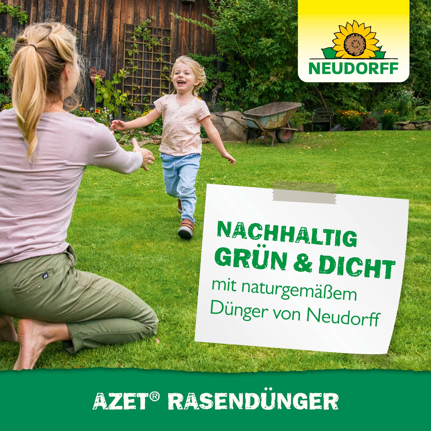 Ein Erwachsener und ein Kind spielen auf einem grünen Rasen vor einem Holzhaus. Der Azet RasenDünger 2,5 kg bis 5 kg von Neudorff Shop sorgt für einen dichten, widerstandsfähigen Rasen - nachhaltig grün und gesund mit natürlichem Dünger.