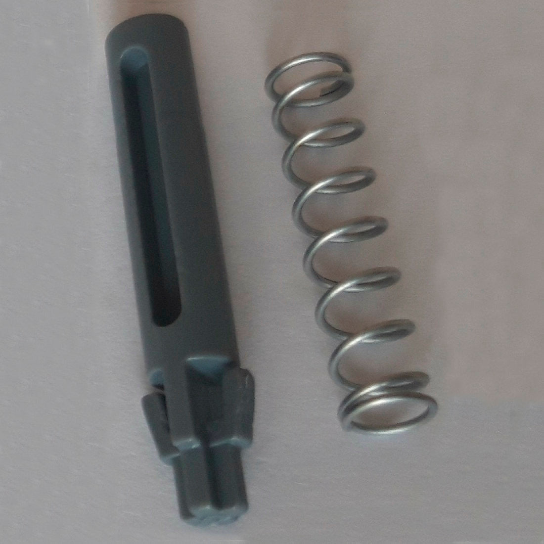 Eine Metallfeder und ein dunkelgrauer zylindrischer Ersatz-Türzapfen mit Rillen und Zacken, Teil des DI Protect Türzapfen & Feder (1 Stück) von Diversey Deutschland GmbH & Co. OHG, sind auf einer hellen Fläche abgebildet und zeigen die robusten Materialien für den DI Protect Trolley.