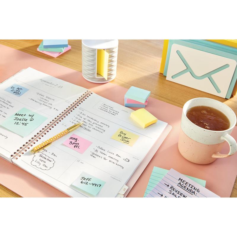 Otvorený plánovač s ručne písanými poznámkami leží na stole vedľa šálky čaju, kartičiek, pera a poznámok Post-it® Notes v žltej farbe (38 mm x 51 mm, 3M Deutschland GmbH) a nádoby.