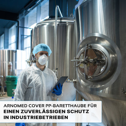 Eine Person, die eine ARNOMED COVER PP-BARETTHAUBE Baretthaube aus PP-Vlies der ARNOWA GmbH und eine Maske trägt, steht vor Edelstahltanks in einem industriellen Hygienebereich und hält ein Tablet in der Hand. Der deutsche Text hebt den zuverlässigen Schutz für die Industrie hervor.