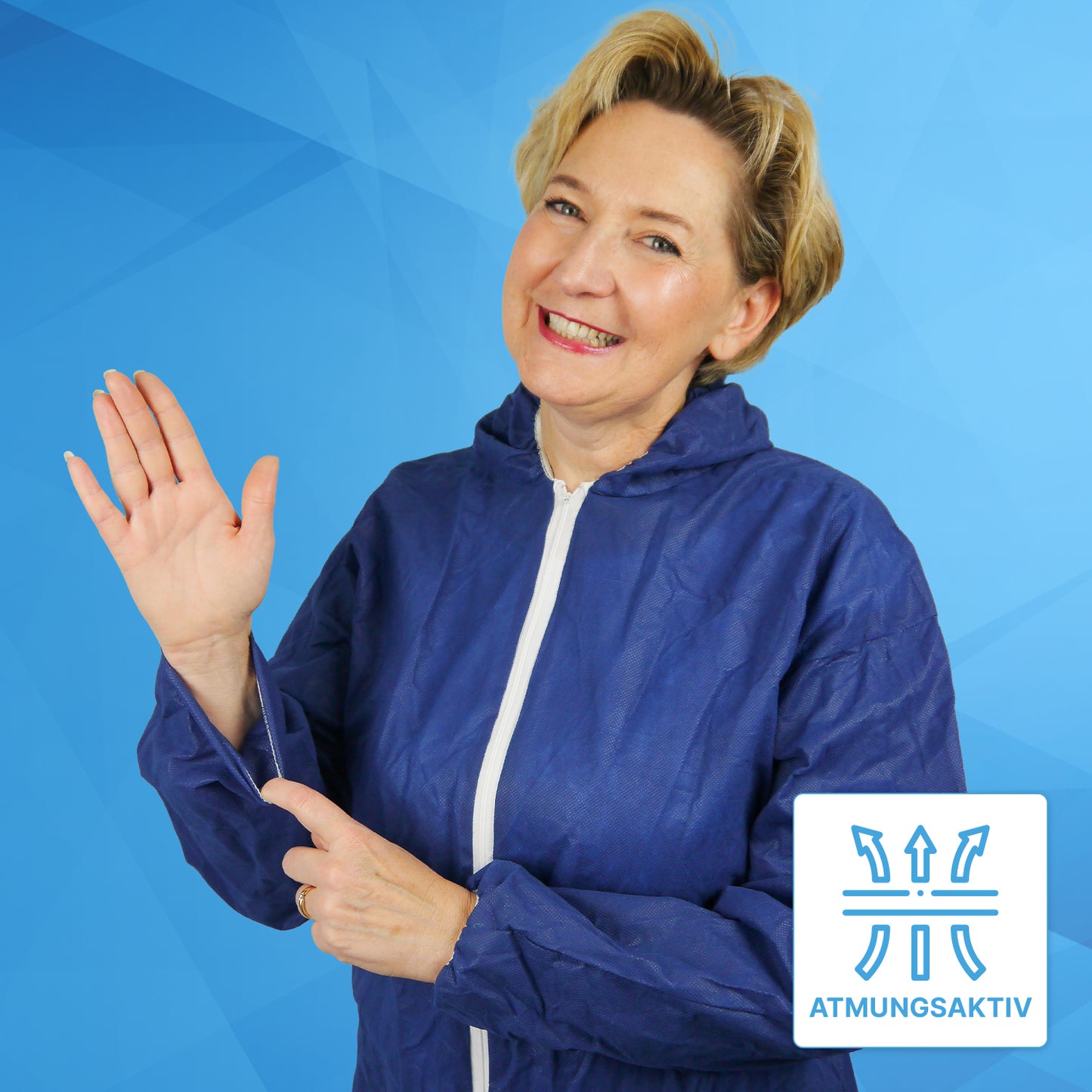 Žena v ARNOMED COVER PP-OVERALL BLUE jednorazovom overale s kapucňou z PP-vlákna od ARNOWA GmbH sa usmieva a ukazuje na rukáv, na ktorom symbol "ATMUNGSAKTIV" zdôrazňuje priedušnú tkaninu pred modrým geometrickým pozadím.