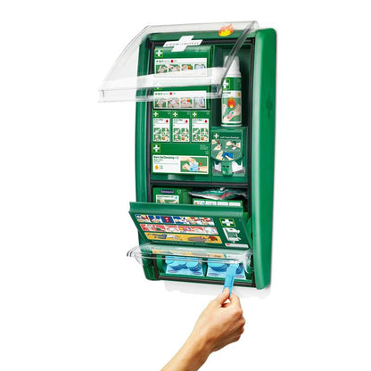 Na stene namontovaná stanica prvej pomoci a popálenín Cederroth od Orkla Wound Care AB je otvorená a ukazuje spotrebný materiál ako obväzy, návody, fľaše na výplach očí a ruku, ktorá vyberá modrú kapsulu na výplach očí z dolnej priehradky. (1 balenie/kartón).