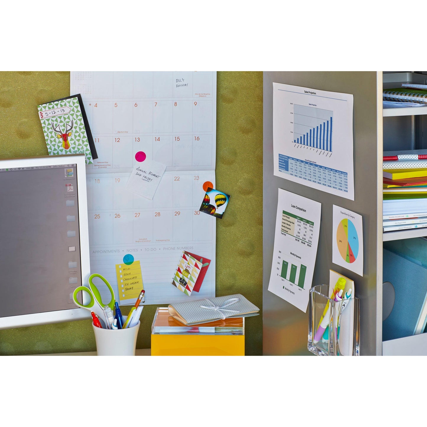 Ein Arbeitsbereich mit einem Wandkalender, mit 3M Scotch-FIX™ Ablösbare Montagequadrate 108-ST64-P befestigten Tabellen, einem Computermonitor, bunten Ordnern, einer Schere in einem weißen Halter, einem gelben Kasten und einem Glas mit Stiften. Notizen werden mit diesen rückstandsfreien Klebepads angeheftet.