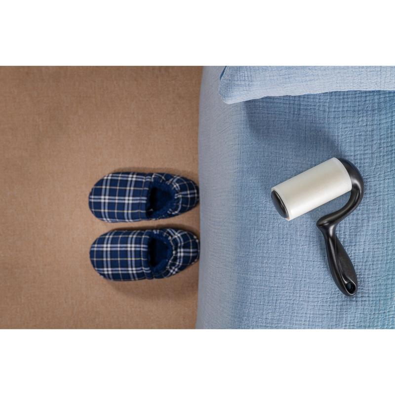 Pár modro kockovaných papúč stojí na béžovom koberci vedľa postele so svetlomodrou prikrývkou, zatiaľ čo Scotch-Brite™ Everyday Clean Fusselroller na ploché povrchy (56 listov, 1/balenie) od 3M Deutschland GmbH leží na posteli pripravený na použitie.