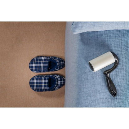 Pár modro kockovaných papúč stojí na béžovom koberci vedľa postele so svetlomodrou prikrývkou, zatiaľ čo Scotch-Brite™ Everyday Clean Fusselroller na ploché povrchy (56 listov, 1/balenie) od 3M Deutschland GmbH leží na posteli pripravený na použitie.