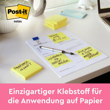 Stoh poznámok Post-it® Notes, žltá, 38 mm x 51 mm (100 listov/blok, 12 blokov/balenie) od 3M Deutschland GmbH leží na stole; vedľa sú štyri lístky s ručne písaným textom pripevnené na liste. Logo Post-it a nemecký slogan sú viditeľné.