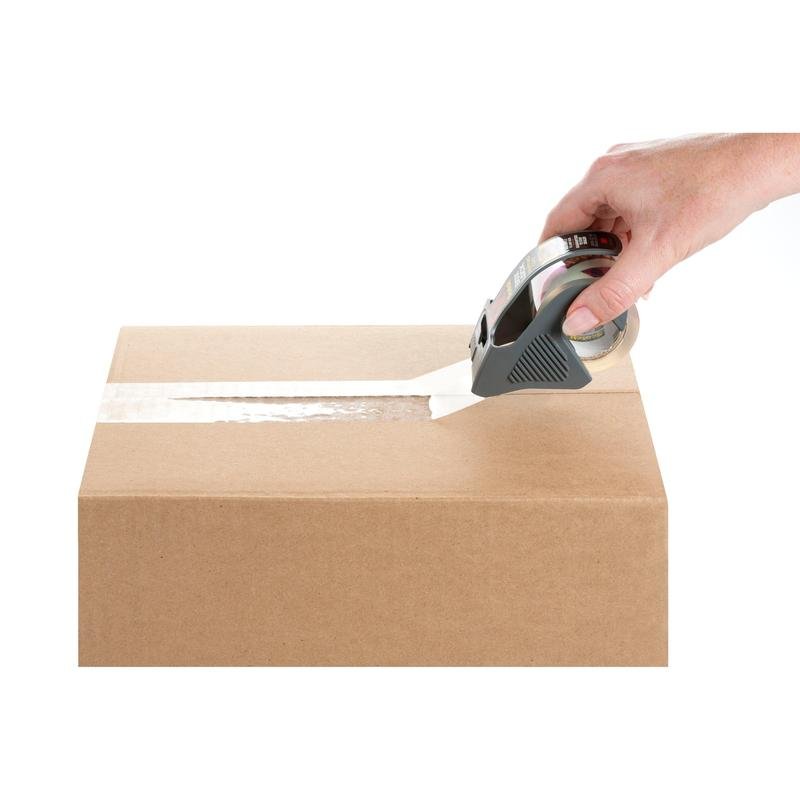 Ruka uzatvára hnedý kartón cez horný šev s použitím Scotch® Box Lock™ baliacej pásky 48 mm x 20,3 m od 3M Deutschland GmbH s dávkovačom pásky, všetko na bielom pozadí.