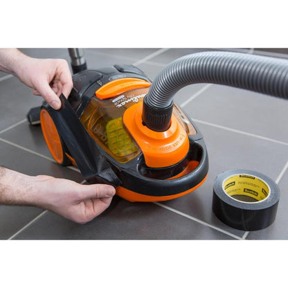 Osoba opravuje popraskané oranžovo-čierne puzdro vysávača s univerzálnou lepiacou páskou Scotch® Extremium™ (3 m x 19 mm) od 3M Deutschland GmbH, pričom rolka leží na sivom dlaždicovom podlaží v blízkosti.