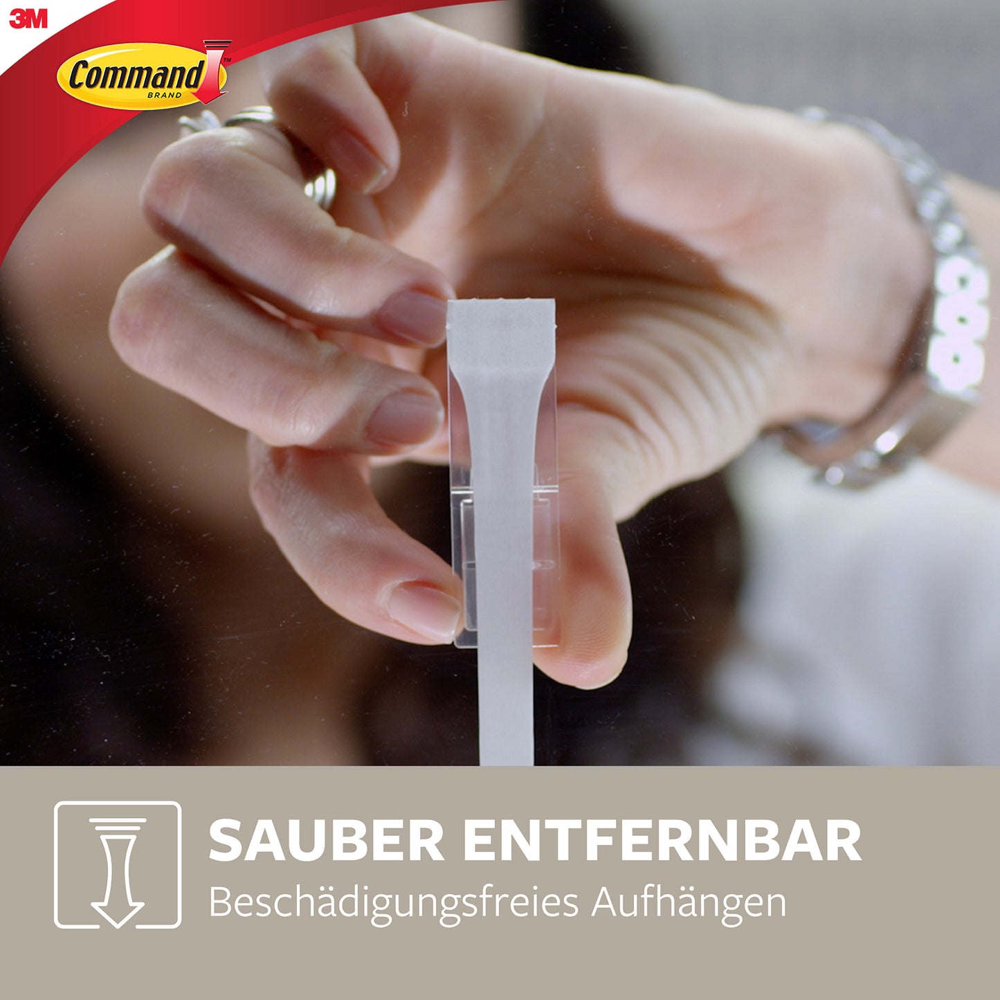 Eine Hand zieht den Klebestreifen eines mittelgroßen Command™ Metallhakens in gebürstetem Nickel, 17034 (1 Haken, 2 Strips) von 3M Deutschland GmbH von einer Glasscheibe. Text: "Sauber entfernbar - Haken ohne Bohren." Command & 3M Logos sichtbar.