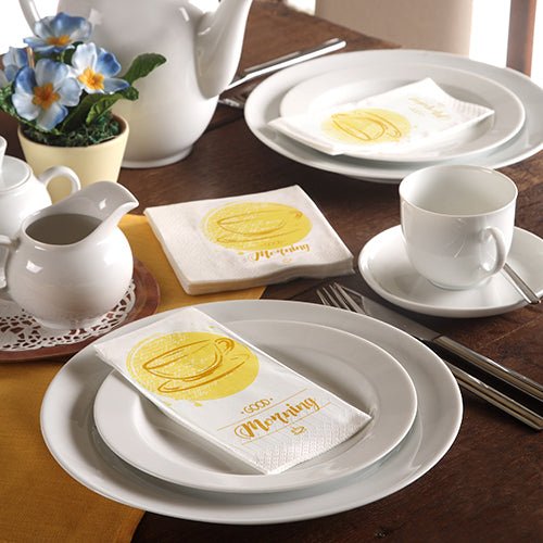 Pekne prestretý stôl s bielym riadom, čajníkom, modrými kvetmi a trojvrstvovými PAPSTAR-Uteráky (33 x 33 cm) z PAPSTAR GmbH so žltým šálkou na kávu a nápisom „Morning“.