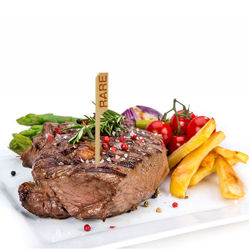 Ein gegrilltes, blutiges Steak, gekennzeichnet mit dem PAPSTAR 250 Steak-Marker (9 cm) der PAPSTAR GmbH, serviert mit Pommes Frites, Spargel, Kirschtomaten am Strauch, roten Zwiebeln und garniert mit Rosmarin und Pfefferkörnern – ganz im Restaurant-Stil.