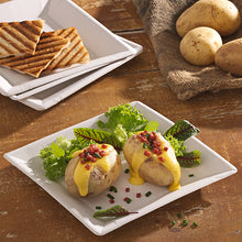 Dve pečené zemiaky so žltou syrovou omáčkou, kúskami slaniny a pažítkou sú podávané na PAPSTAR papierovom tanieri štvorcového tvaru 22,5 cm v "pure" dizajne od PAPSTAR GmbH. Listová zelenina sprevádza jedlo, v pozadí je grilovaný chlieb a celé zemiaky.