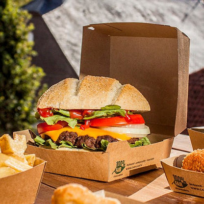 Cheeseburger so šalátom, paradajkou, cibuľou a syrom čedar leží vonku v PAPSTAR GmbH Kartónová krabička na hamburgery (9 × 18,5 × 18,5 cm, „100 % Fair“, 25 ks). Hranolky a ďalšie prílohy sa podávajú samostatne vedľa nich.