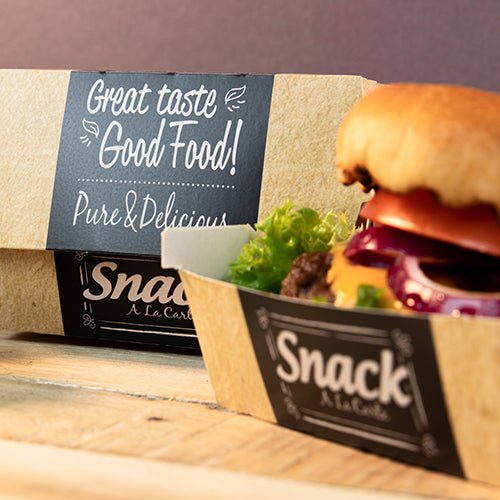 Kartónový podnos s nápisom "Snack A La Carte" obsahuje hamburger so šalátom, paradajkou a cibuľou. V pozadí je PAPSTAR 50 burgerových krabíc, kartón "pure" "Good Food" od PAPSTAR GmbH: Dobrý vkus Good Food! Čisté a chutné.