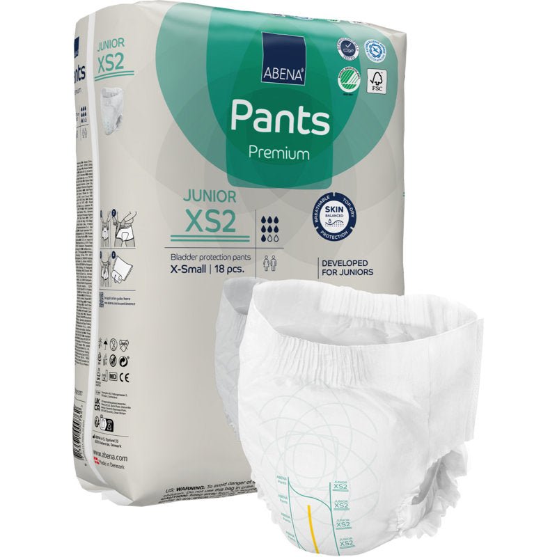 Balenie ABENA Pants Junior Premium, veľkosť XS2 od spoločnosti Abena Re-Seller GmbH, je zobrazené s nerozloženou plienkou v popredí. Balenie béžovej farby so zelenými a modrými akcentmi obsahuje 18 kusov veľkosti X-small.