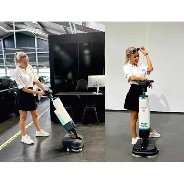 Zwei Frauen in weißen Hemden und schwarzen Röcken benutzen die Arcora International GmbH Tiger 40 Bodenreinigungsmaschine | Karton (1 Stück) in Innenräumen; eine bedient die Maschine, während die andere lächelnd ihre professionelle Reinigung präsentiert.
