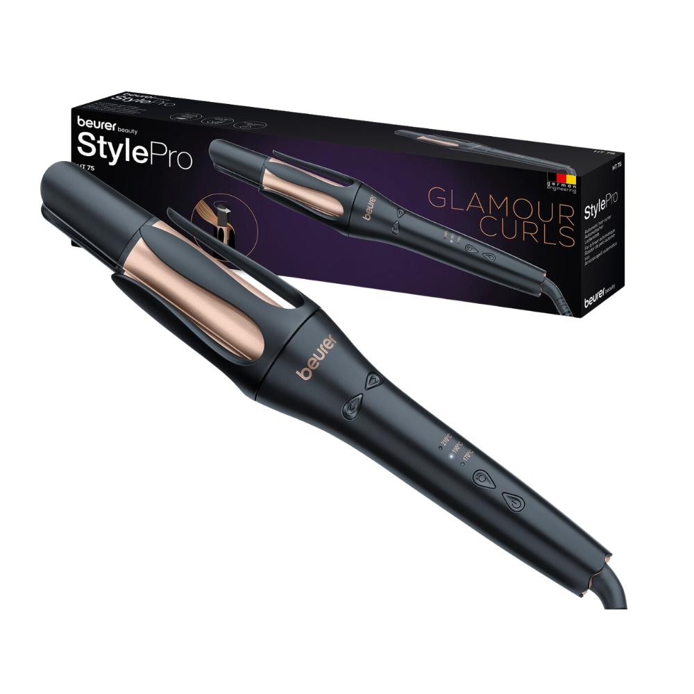 Elegantný automatický kulmofén HT 75 od Beurer GmbH v čiernom a ružovozlatom dizajne je vidieť spolu s jeho balením s nápisom „Glamour Curls“. Automatický kulmofén má digitálne ovládacie prvky na rukoväti a 4-násobný ionový výstup. Na krabici je zobrazený obrázok kulmofénu a značka.
