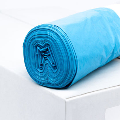 Rolka modrého DEISS LDPE vreca na odpad Typ 60, 20772, 70 litrov od EMIL DEISS KG (GmbH + Co.) leží na bielej krabici. Tieto odolné vrecia, známe svojou pevnosťou v ťahu, sú úhľadne zrolované, aby bola viditeľná vrstva recyklovaného materiálu. Pozadie zostáva jednoduché a minimalistické.