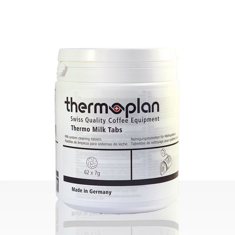 Biely plastový kontajner s nápisom "Thermoplan Thermo Milk Tabs, čistiace tablety pre espresso stroje | Balenie (62 kusov)" od Diversey Deutschland GmbH & Co. OHG, na hygienické čistenie, ukazuje "62 x 7g", "Vyrobené v Nemecku" a viacjazyčné informácie.