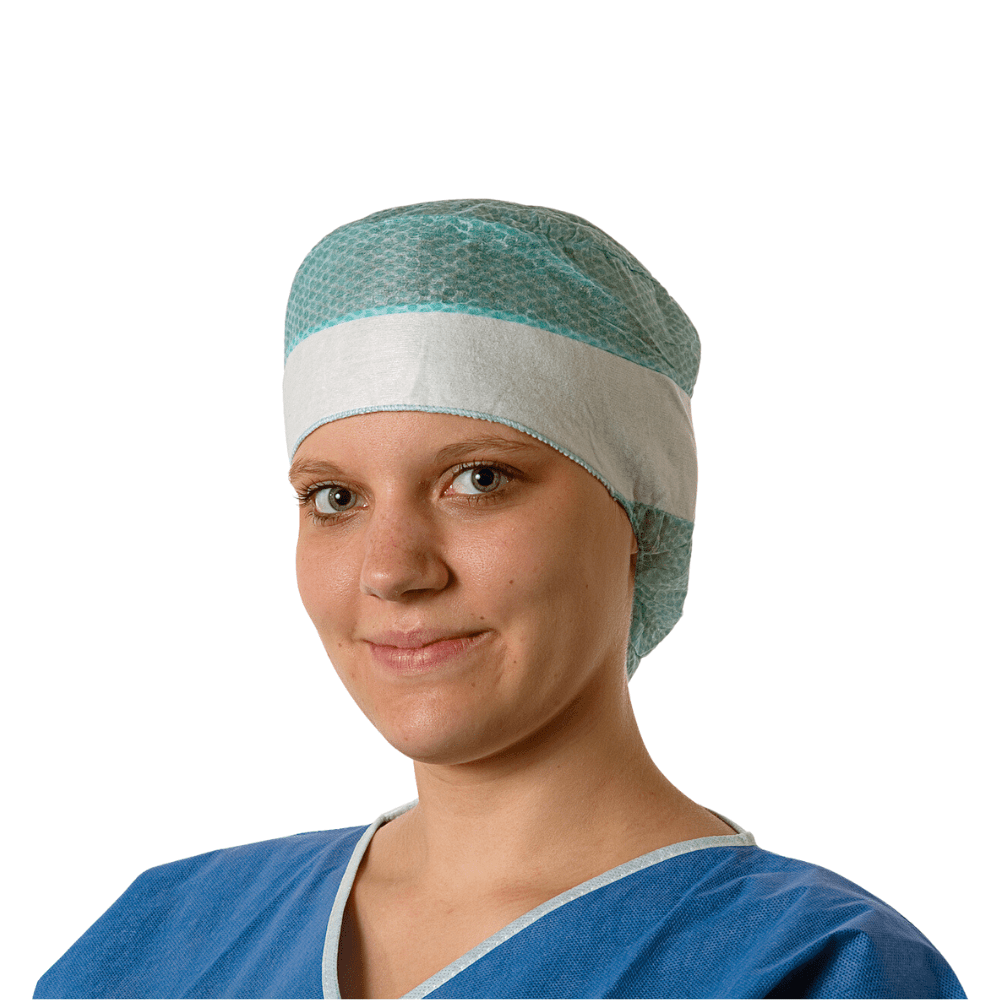 Mladá lekárka má na sebe modrý operačný plášť a jednorazovú čiapku Hartmann Foliodress® Cap Comfort Form Plus z priedušného viskózového rúna a jemne sa usmieva do kamery. Pozadie je jednoducho biele.
