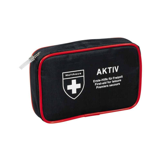 Kompaktná čierna lekárnička s červeným lemovaním a zipsom, s logom bieleho kríža a nápismi „Holthaus Medical AKTIV“ a „Erste-Hilfe für Freizeit / First-aid for Leisure / Premiers secours“ na prednej strane. Ideálna na cesty aj do domácnosti.
