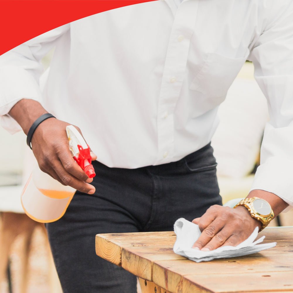 Osoba v bielej košeli používa krabicu WypAll® X60 General Clean (Biela, 10x126 listov) od Kimberly-Clark GmbH na čistenie dreveného povrchu. Viditeľný je iba jej trup a ruky. Fotografia má v hornej časti červený zakrivený okraj.