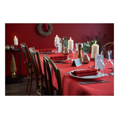 Ein Esstisch ist mit Dunicel-Tischdeckenrollen (1,18 m x 10 m) der Duni GmbH und passenden Servietten, weißen Tellern, Weingläsern, Kerzen und einer Menükarte gedeckt. Braune Stühle umgeben den Tisch vor roten Wänden mit festlicher Weihnachtsdekoration – perfekt für große Veranstaltungen.