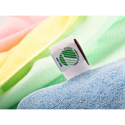 Detailný pohľad na látkovú etiketu na uteráku Vileda Professional MicroTuff Plus so symbolom Nordic Swan Ecolabel. Uterák má jemné farebné tóny v žltej, ružovej, zelenej a modrej farbe s viditeľnou textúrou a je preto ideálny pre profesionálne čistenie. Je vyrábaný spoločnosťou Vileda GmbH a je známy ako udržateľná mikrovláknová utierka.