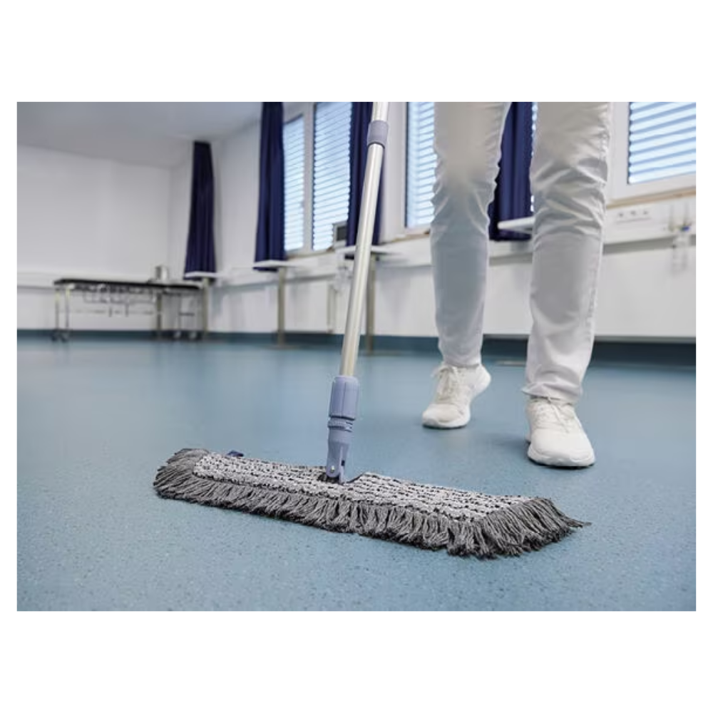 Osoba v bielych topánkach a nohaviciach utiera modrú podlahu v miestnosti so zatvorenými žalúziami a modrými závesmi pomocou Vileda GmbH Professional Swep Duo r-MicroCombi Mop - 50 cm. V blízkosti je skladací stôl a pod oknami je radiátor.