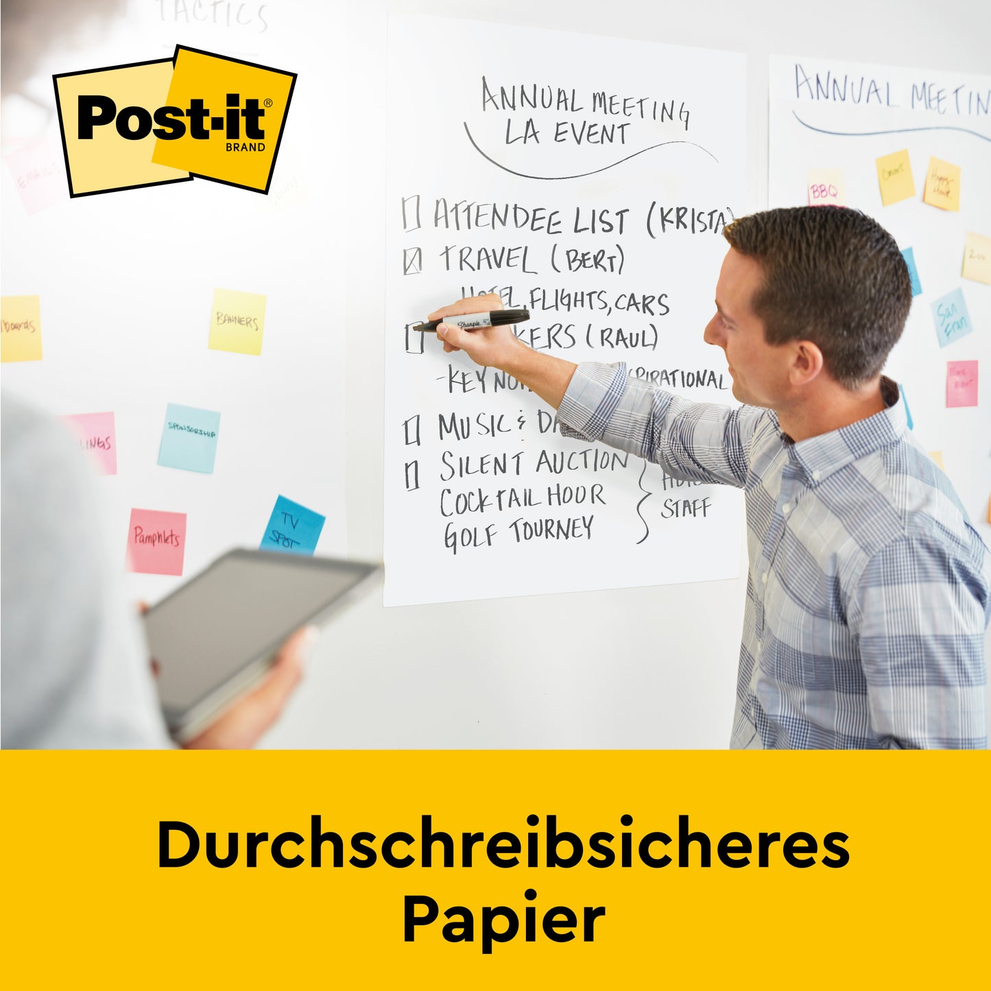 Ein Mann schreibt auf eine 3M Post-it® Super Sticky Meeting Chart (63,5 x 76,2 cm, selbsthaftend, 30 Blatt/Block), die an der Wand befestigt ist, während ein anderer ein Tablet hält. Die weiße Karte zeigt Notizen für eine Veranstaltung. Text: "Durchschreibsicheres Papier.