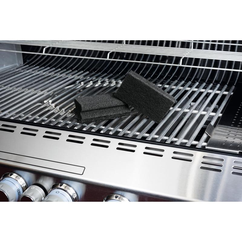 Scotch-Brite® Grill Griffschwamm od 3M Deutschland GmbH leží na nerezovom grile a zdôrazňuje jednoduché čistenie grilu. Na rošte sú viditeľné čierne špongie, grilové gombíky a otvorený kryt.